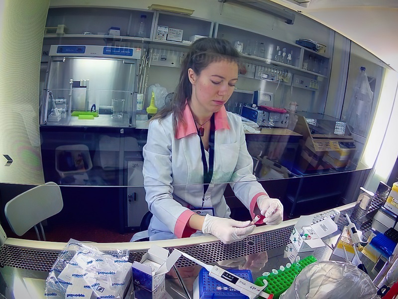 Researcher Alisa Kazarina working in a laboratory, handling samples under a fume hood.